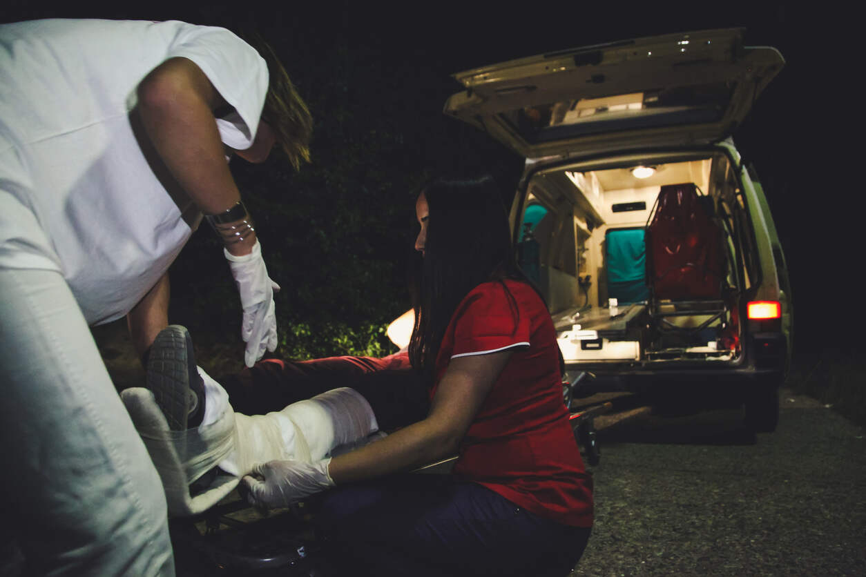 Paramedics aiding an injured person near an ambulance at night, symbolizing a catastrophic injury.