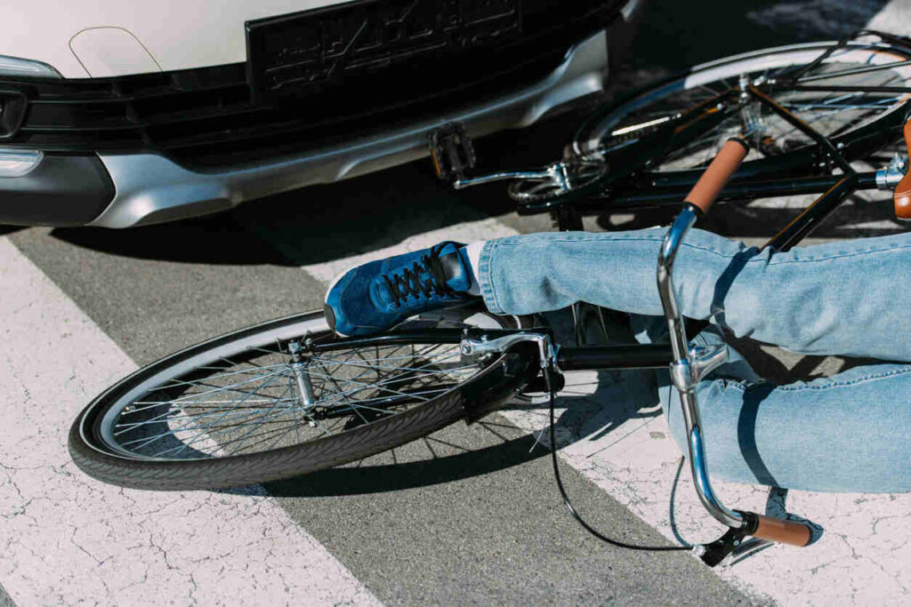 A bicycle and person's legs on the ground next to a car bumper after a hit-and-run accident in Chicago.