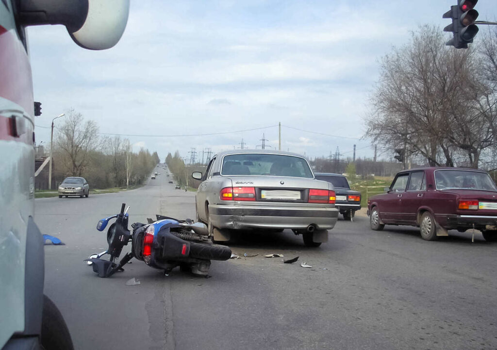Motorcycle accident caused by car's blind spot at an intersection, with a silver car and damaged motorcycle on the road.